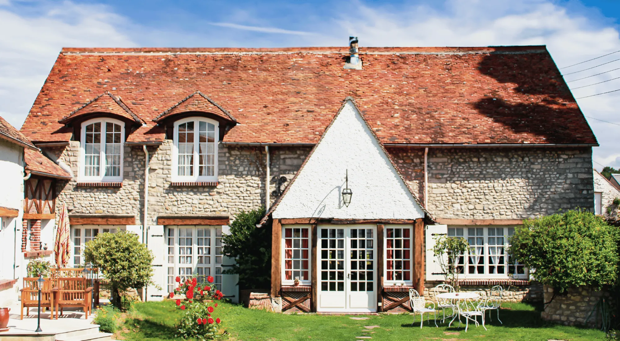 Le gîte depuis son jardin, sa façade de pierre et son pignon blanc