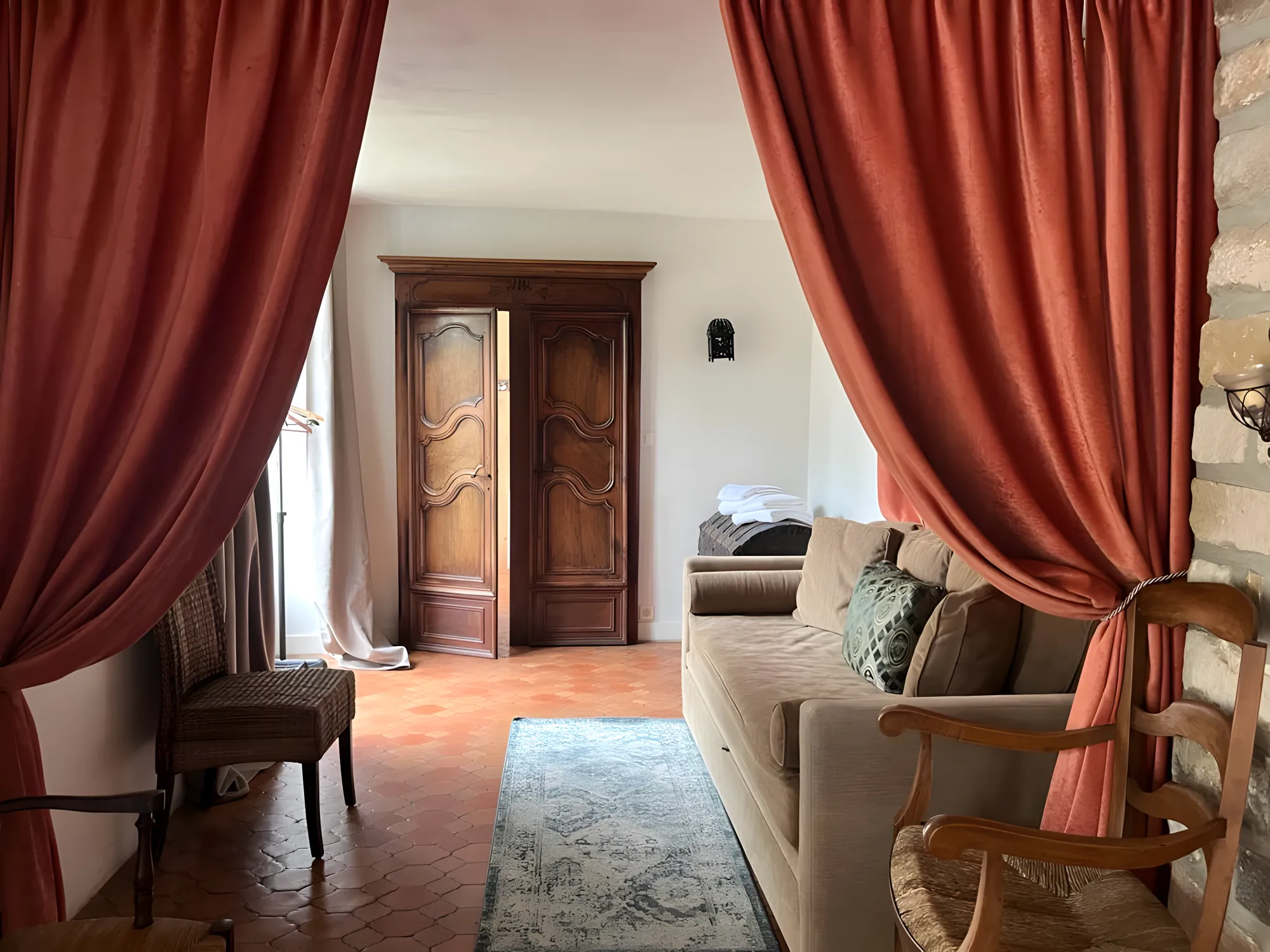 Un salon du gîte, rideaux rouille, canapé beige et armoire ancienne